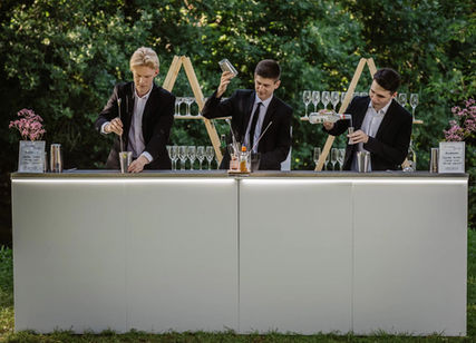 Professional event bar staff in Los Angeles working a multi-bartender cocktail station at an outdoor event, representing experienced bartenders, mixologists, and baristas serving weddings, corporate events, and upscale social gatherings. The image highlights coordinated bar operations, craft cocktail preparation, glassware management, and efficient high-volume beverage service. Ideal for clients hiring event bar staff in Los Angeles who need reliable bartenders, skilled mixologists, and professional baristas capable of handling large guest counts, outdoor venues, and fast-paced event environments with consistent service quality.