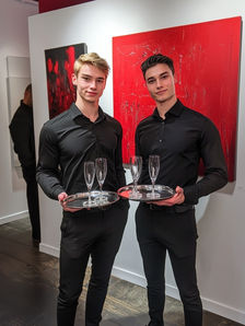Las Vegas event model servers holding champagne trays at a modern gallery-style event, dressed in coordinated black attire for a clean, upscale look. The image highlights professional Las Vegas event model servers supporting private receptions, art exhibitions, corporate mixers, and invitation-only brand events. These servers combine attentive beverage service, confident guest interaction, and polished presentation to maintain event flow, visual balance, and elevated service standards across luxury and corporate events in Las Vegas.
