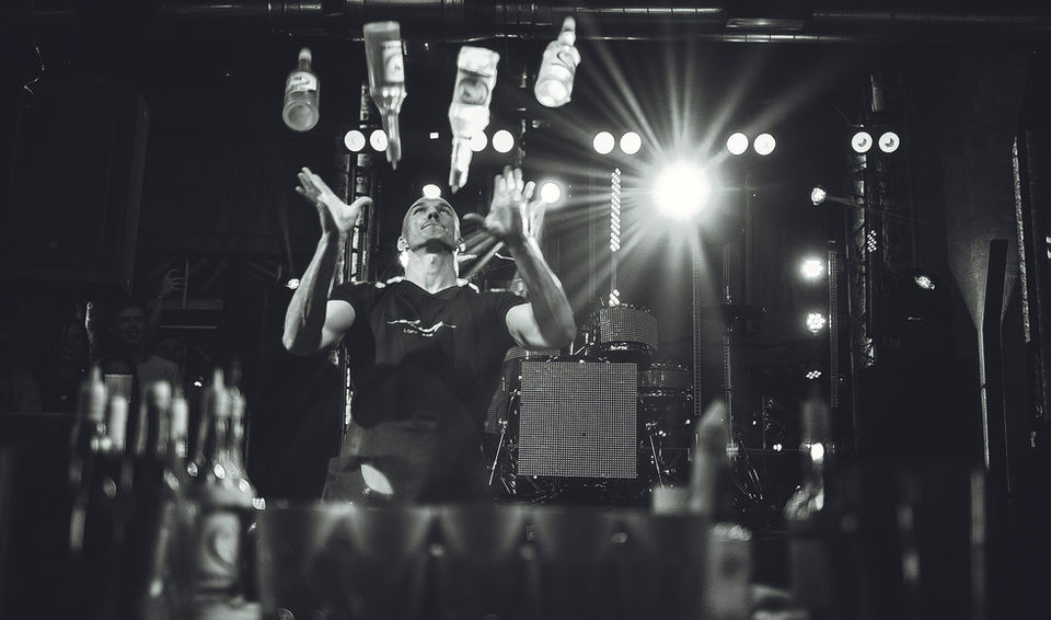 A flair bartender in Los Angeles performs an advanced bottle-juggling routine on stage during a live entertainment event. Flair bartending entertainment combines high-energy bottle tricks, interactive cocktail performances, premium beverage service, and bar entertainment for corporate events, gala dinners, private parties, cocktail receptions, and VIP celebrations.