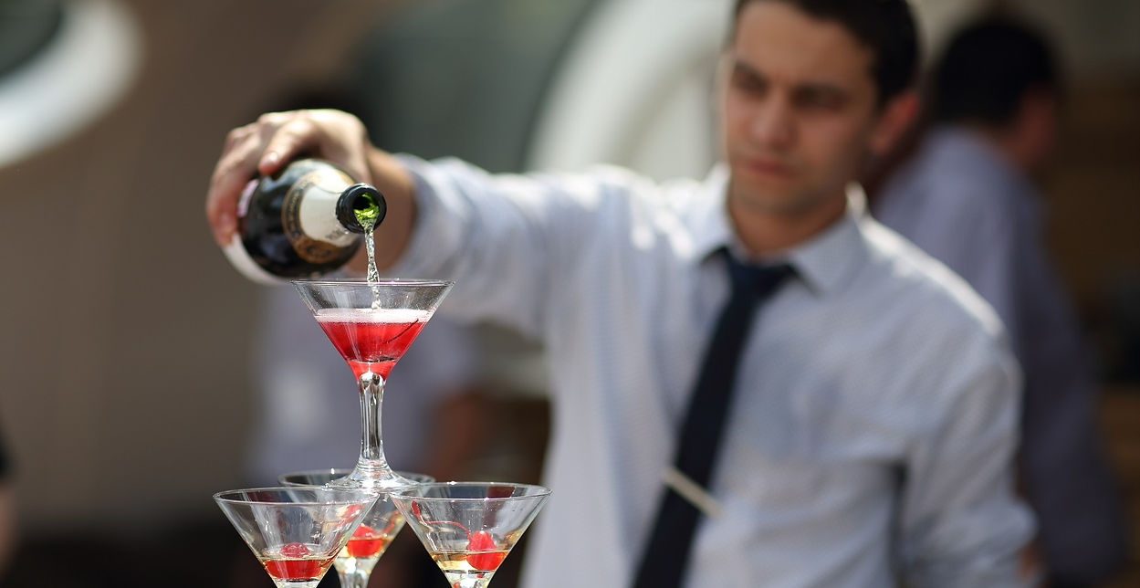 Professional bartender in Los Angeles pouring champagne into a tower of cocktail glasses at a luxury event — upscale bar staffing for weddings and private parties.