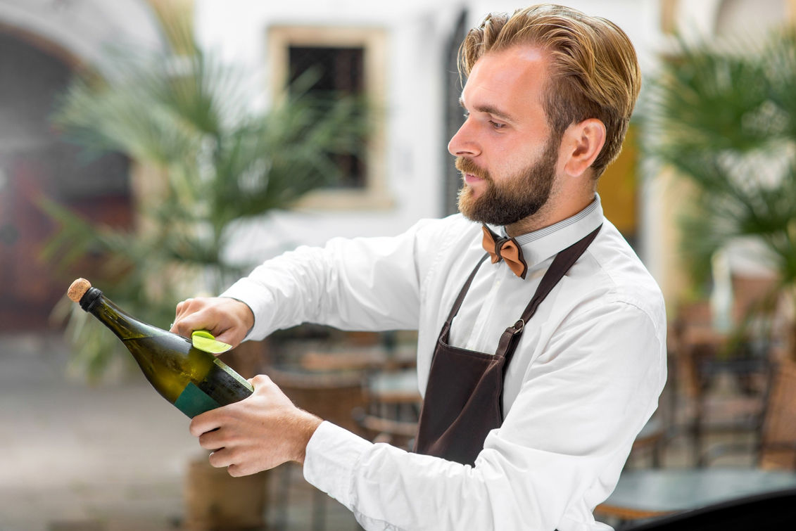 Professional event bar staff member in Los Angeles opening a champagne bottle at a private event, representing experienced bartenders, mixologists, and baristas available for weddings, corporate functions, brand activations, and upscale social gatherings. The image highlights refined beverage service, champagne presentation, and guest-facing professionalism behind a styled event bar. Ideal for clients hiring event bar staff in Los Angeles who need reliable bartenders, skilled mixologists, and professional baristas capable of delivering consistent, high-quality beverage service and smooth guest flow in fast-paced event environments.