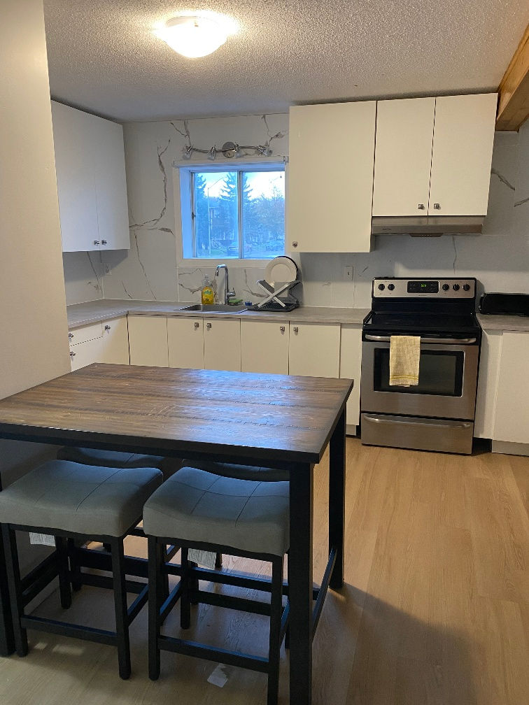 Cuisine commune équipée avec cuisinière, réfrigérateur, évier et table à manger dans une maison de chambres à Jonquière.