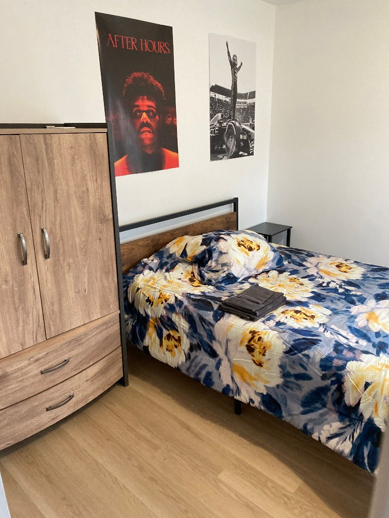 Chambre meublée à louer à Jonquière avec lit double, armoire en bois et literie fleurie.