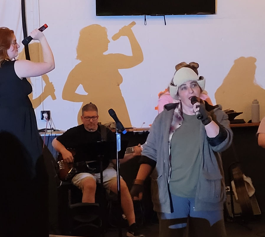 Rachel Boehm singing as The Troll during a dress rehearsal of 'Monstersongs,' with the band and Siren Sisters in the background.