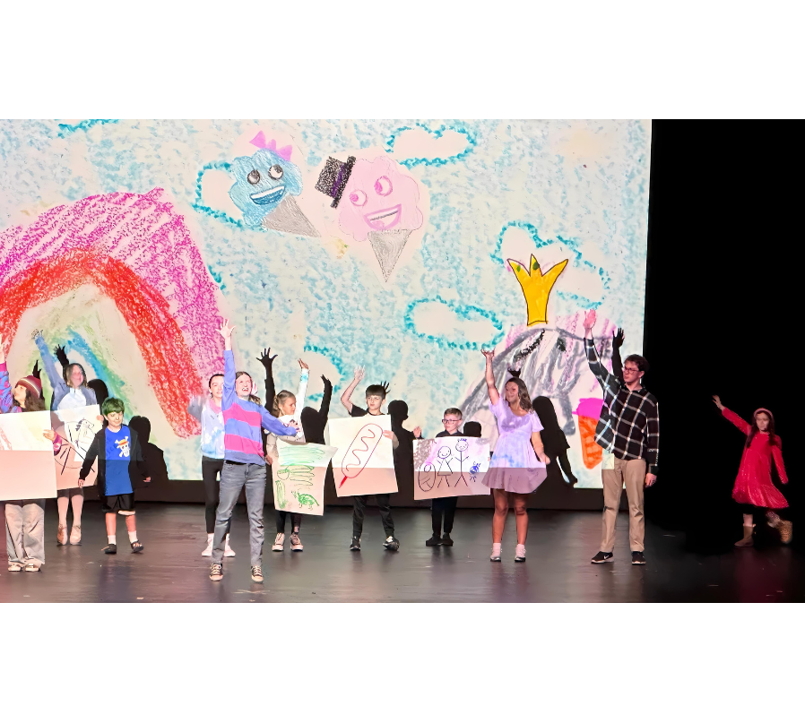 Junie B. Jones and the other kids holding signs with different pictures drawn on them, all with their arms raised high. The background features a rainbow, two ice cream cones with hats or bows, and a dolphin wearing a crown.