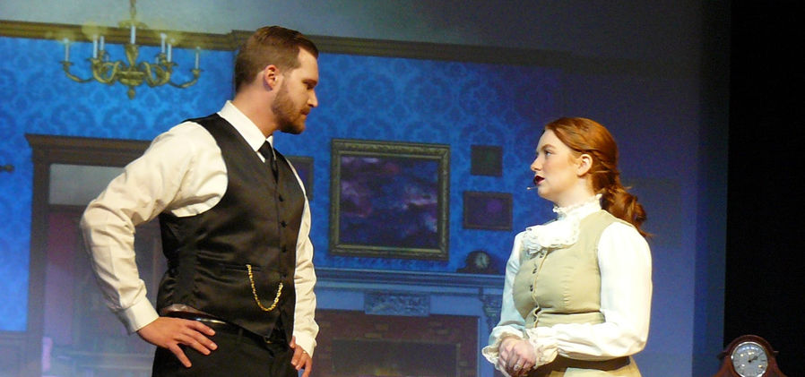 George (Casey Long) and Winifred (Emily Turner) stand facing each other, both with serious expressions on their faces.