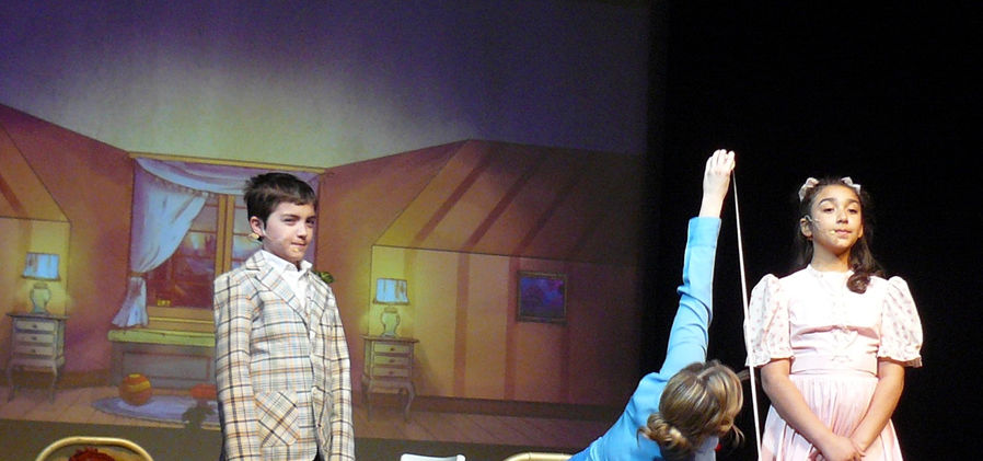 Mary Poppins measures Jane with a tape measure, while Michael stands nearby, watching curiously.