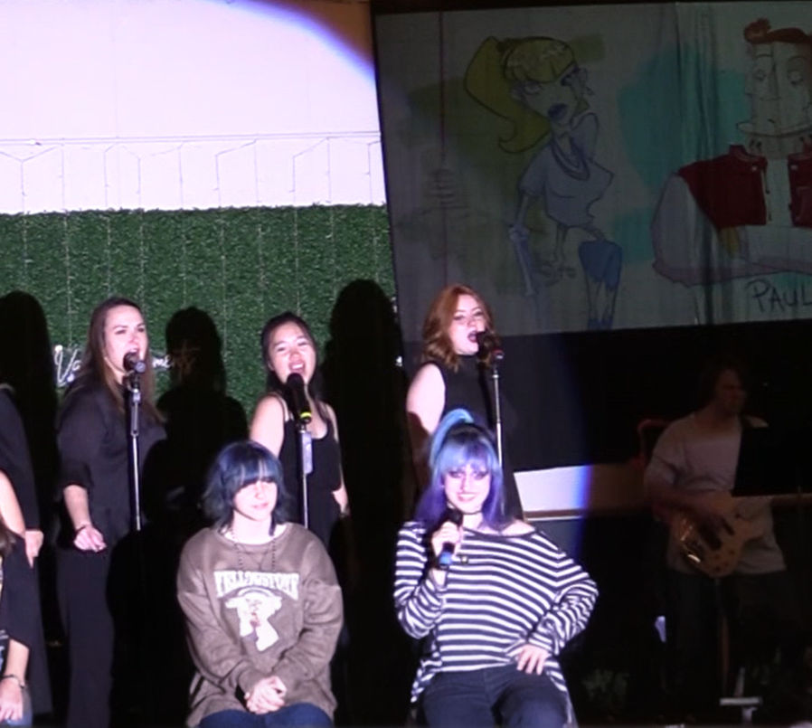 Harper Moore as Vampire Girl and Risa Norbury as Zombie Girl sing to an audience member, with the Siren Sisters singing in the background during a scene from 'Monstersongs.