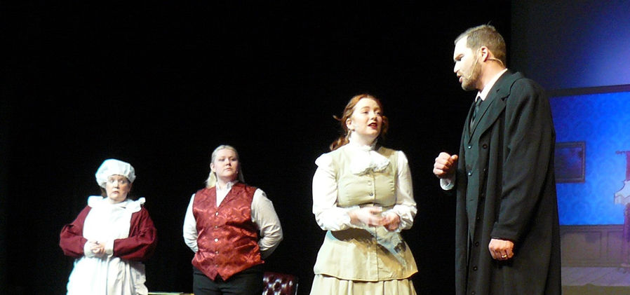George and Winifred Banks talk intently while Mrs. Brill and Robertson Ay stand in the background, observing.