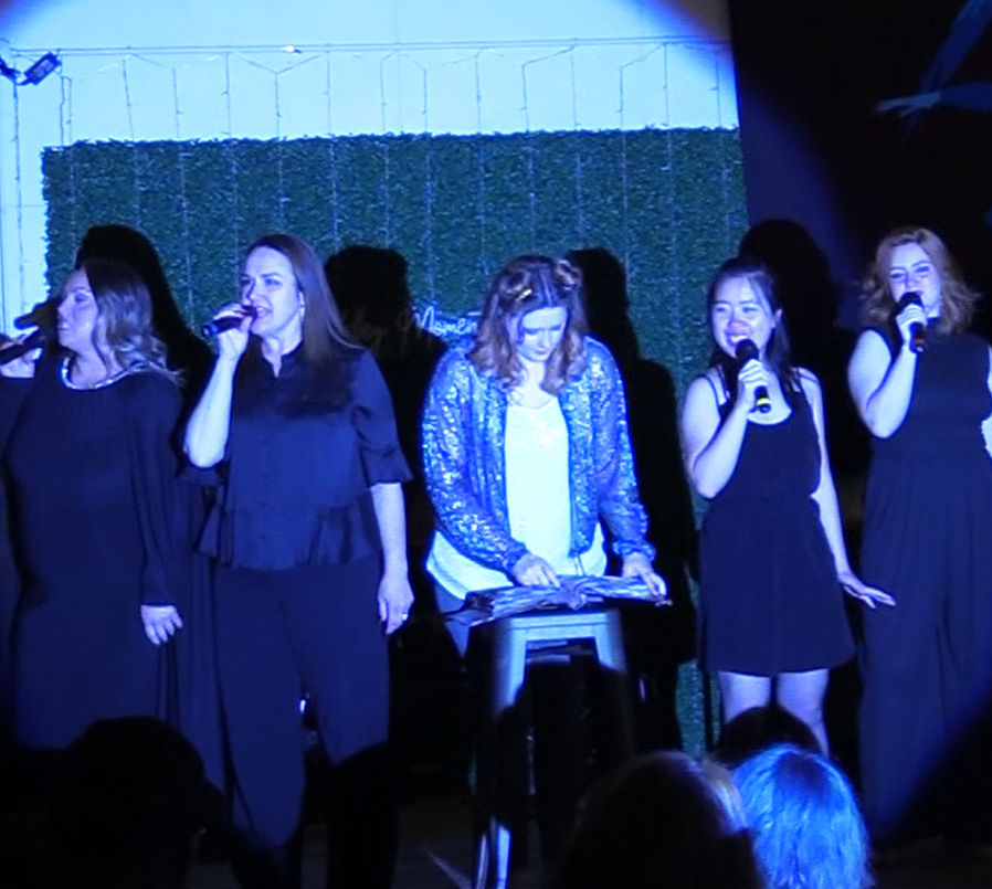 Alt text: "The Siren Sisters, played by Jessica Fletcher, HeatherAnne Norbury, Ruthie Wu, and Emily Turner, sing together around The Kid, played by Noelle Postelthwait, during a scene from 'Monstersongs.'"