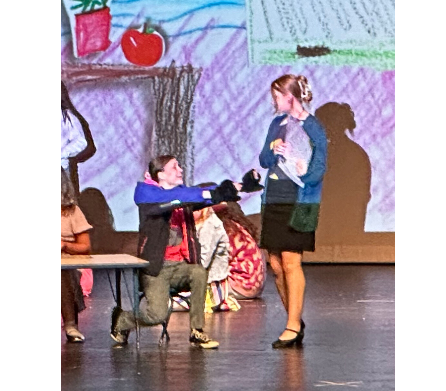 Junie B. Jones, wearing her mittens, sitting at a table and reaching up to Mrs. with an eager expression.
