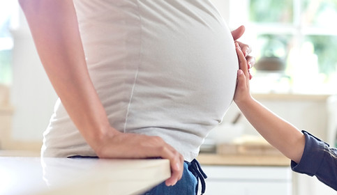 Side view of a mother's pregnant belly with her child's hand placed on it, as well as her own.
