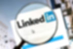 Magnifying glass over LinkedIn login screen, highlighting logo. Blue and white color scheme. Blurred building background.