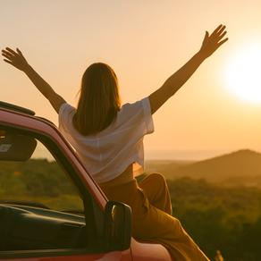 A woman sits on a red car at sunset, arms raised in joy during her ultimate weekend getaway from Hyderabad. With hills and greenery around, she travels smarter using the POOLit carpool app 