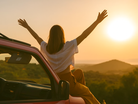 A woman sits on a red car at sunset, arms raised in joy during her ultimate weekend getaway from Hyderabad. With hills and greenery around, she travels smarter using the POOLit carpool app
