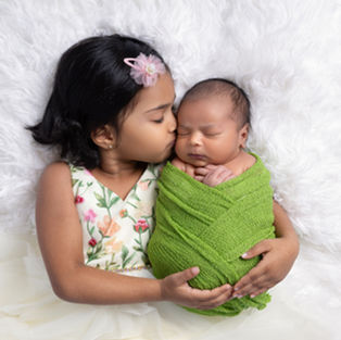 Older sister kissing a newborn baby wrapped in a green blanket during a newborn photography session in Pleasanton, California.