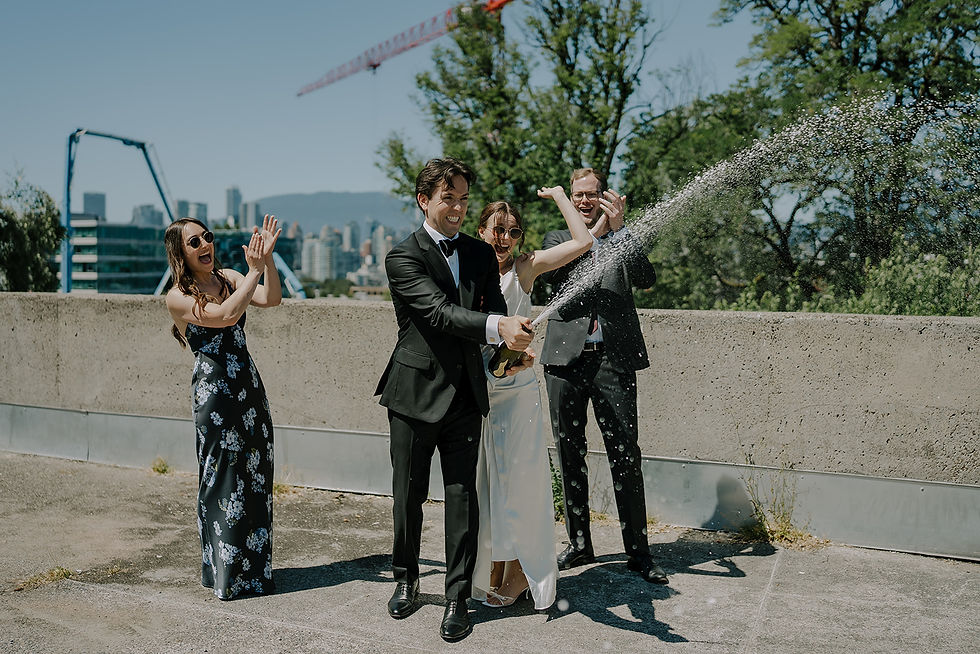 Wedding guests spray champagne outdoors, smiling in formalwear with city skyline and trees in the sunny background. Intimate, moody, City-Hall Civil Wedding photography