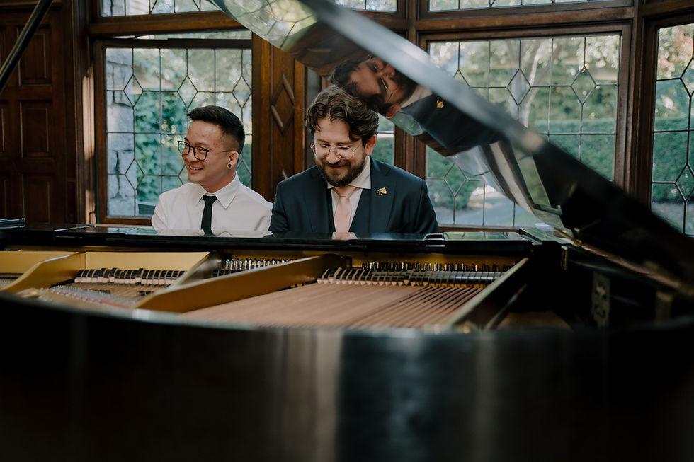 Two men smile beside a grand piano in a wood-paneled room with stained glass windows and warm natural light. Aberthau Mansion in Vancouver, Heartfelt, moody and timeless Wedding Photography.
