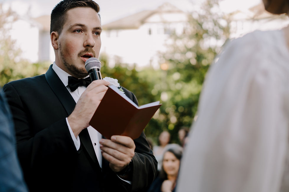 Vows Exchange: Groom holding his book during their wedding vows, framed by lush greenery and the sunset.