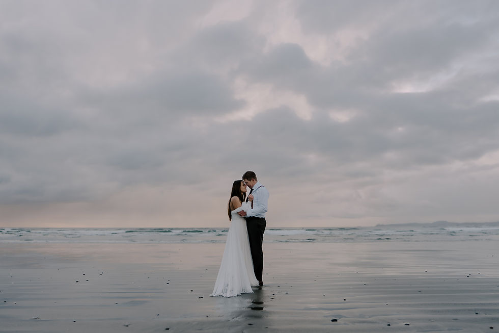 Couple embracing on a cloudy beach, reflecting softly on wet sand. Romantic, serene atmosphere with pastel sky and gentle waves.  Vancouver Moody Romantic intimate Wedding Photographer.