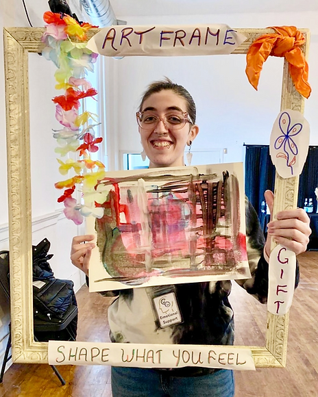 Savannah Dasilva, Registered Psychotherapist (Qualifying) in Toronto holding an artwork in left hand and an art frame in right hand.