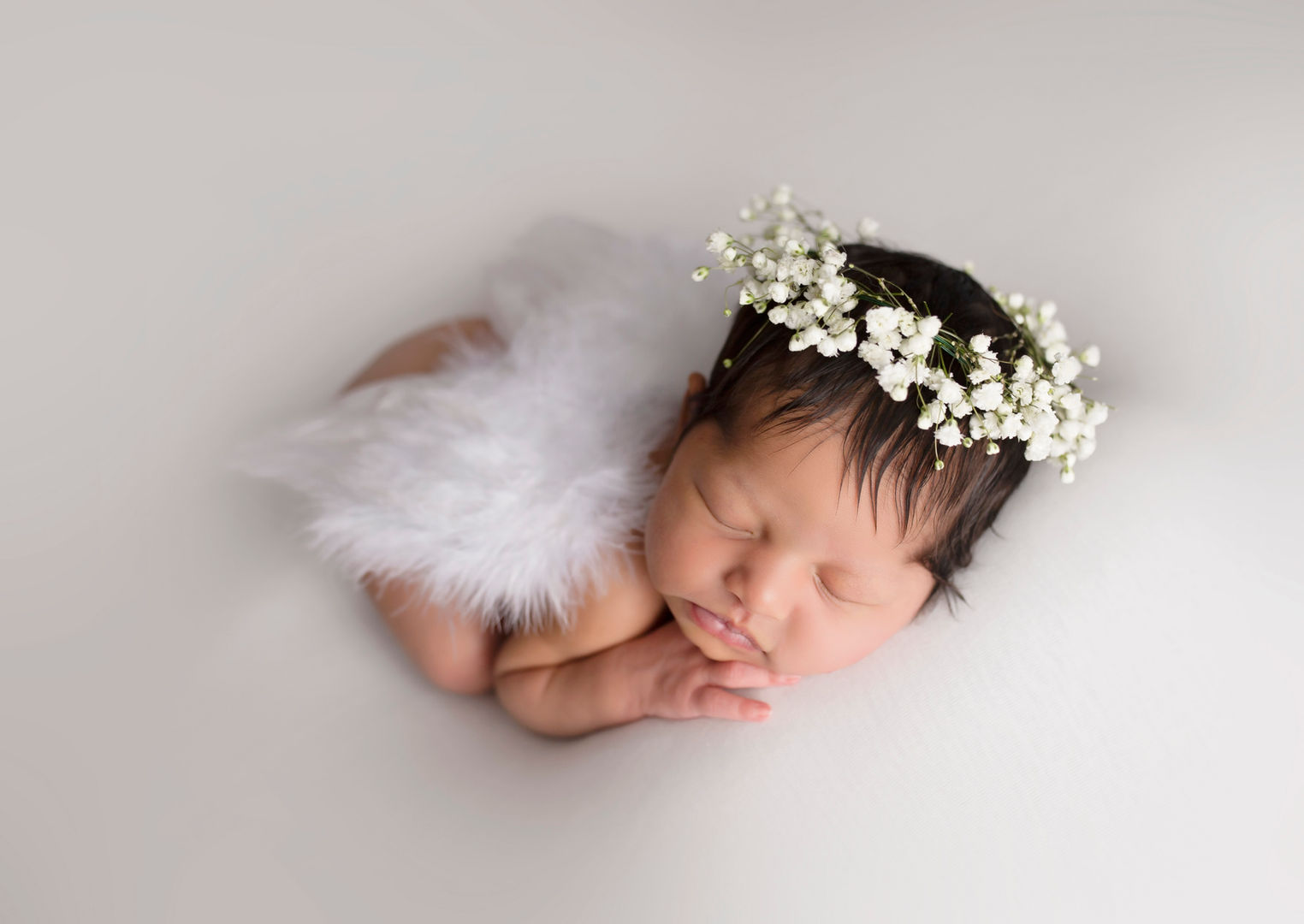 Sleeping newborn baby wearing white feather wings and floral crown.