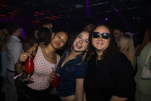 Three people smiling at a party with drinks.