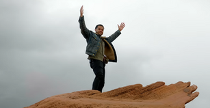Man standing on large hand sculpture with arms raised.