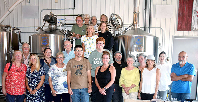 Group of smiling adults posing in a brewery beside stainless steel tanks in an industrial room, casual clothes and cheerful mood