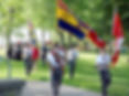 People march in a park carrying military and Canadian flags; a yellow flag reads Fort Malden, Bancroft, on a sunny day.