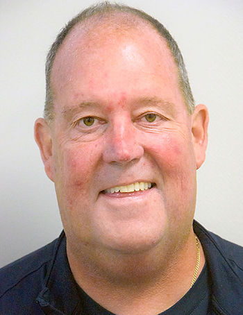 Smiling middle-aged man in a navy shirt and gold chain, posed against a plain light background.