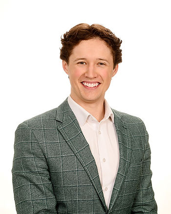 Smiling young man in a green plaid blazer and white shirt posed against a white background.