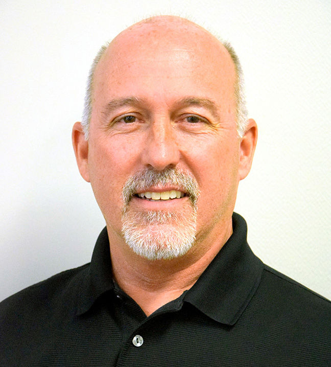 Smiling bald man with gray goatee in a black polo shirt posed against a plain white background.