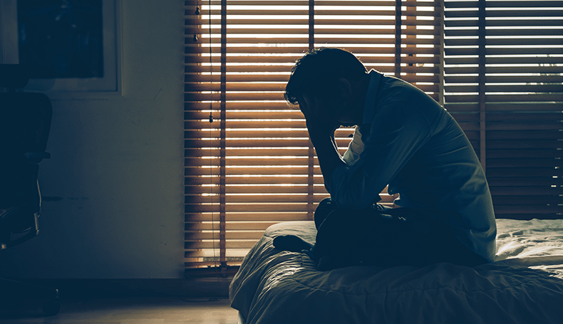 un hombre deprimido sentado en la cama en una habitaciòn oscura