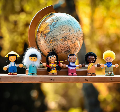 Vor eine Weltkuge stehen unterschiedliche Puppen und halten sich die Hände
