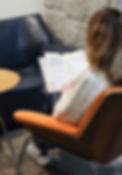 A woman sitting in an orange chair, reading a book. View is from behind the person.