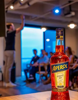 A bottle of alchohol being presented, in the back there is a man speaking