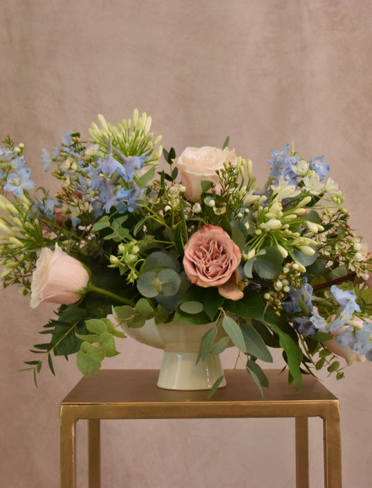 Wedding reception flowers, from an Oxfordshire florist. Asymmetrical floral arrangement in white footed ceramic bowl. Blue delphiniums, white agapanthus, light pink roses, cappuccino roses with eucalyptus foliage.