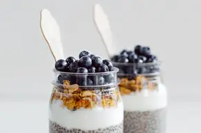 Healthy breakfast jars with chia seeds, yogurt, granola, and fresh blueberries on a clear background, demonstrating a transition from business to health lifestyle.