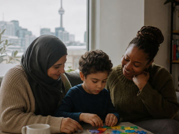 Two mothers helping a boy with a puzzle