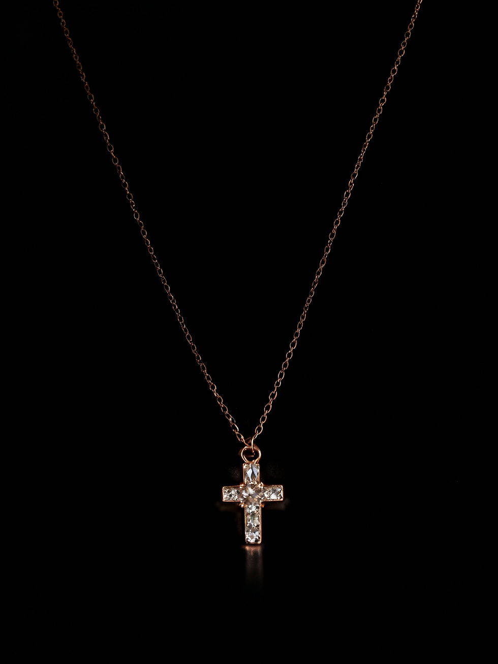Gold cross pendant necklace with clear crystals against a black background.