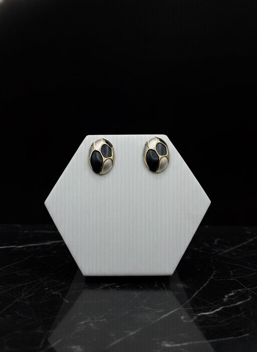 Pair of black and gold earrings displayed on a white hexagon stand.