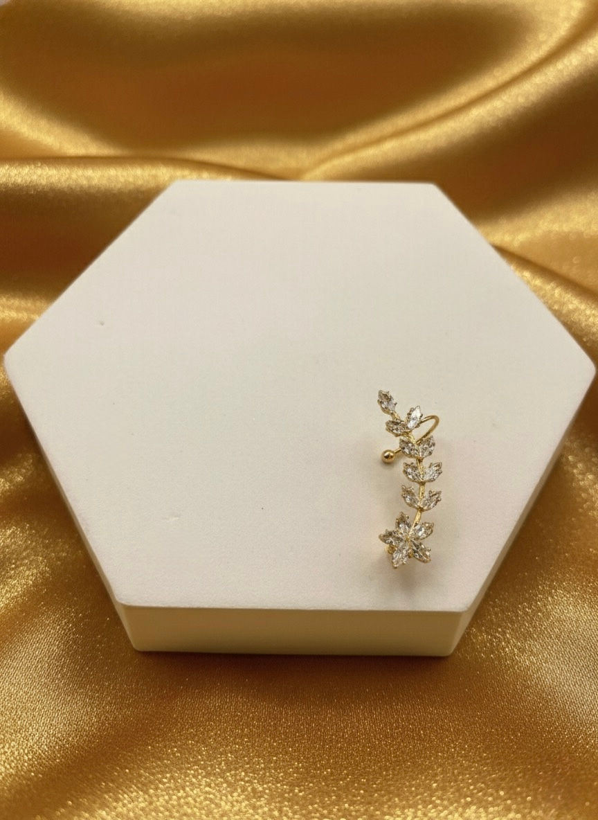 Golden leaf-shaped earring sits on white display, Lavish Jewellery