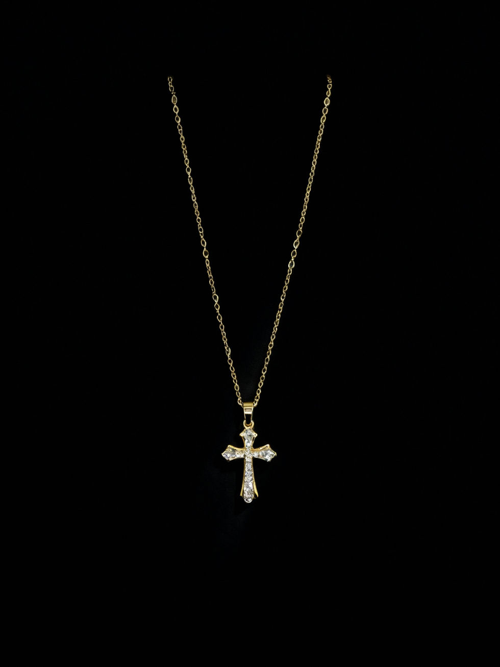 Golden cross pendant necklace hanging against a black background. Lavish Jewellery.