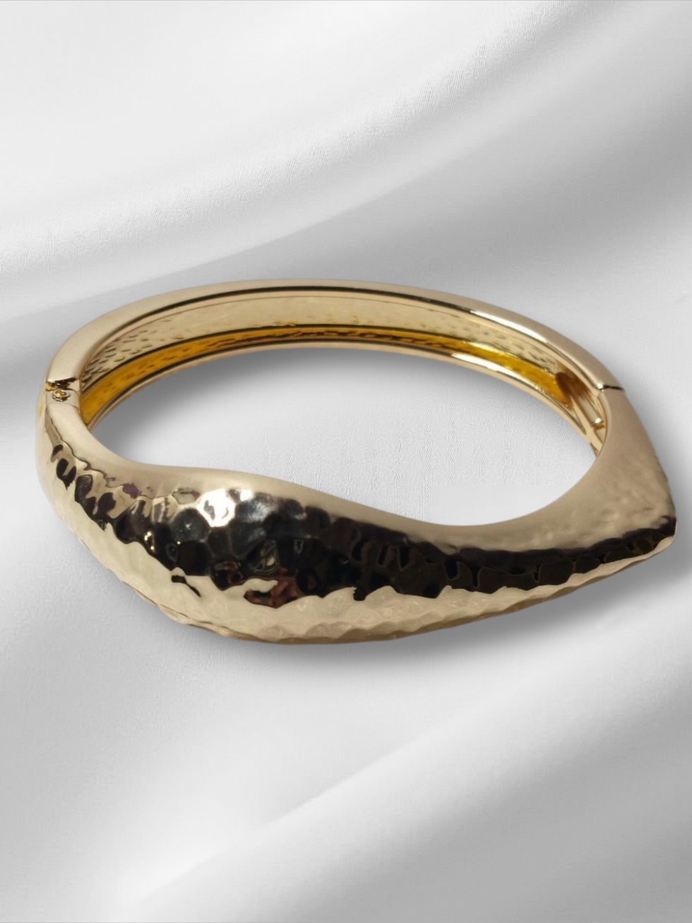 Gold bracelet on white silky cloth. Lavish jewellery, elegant design.