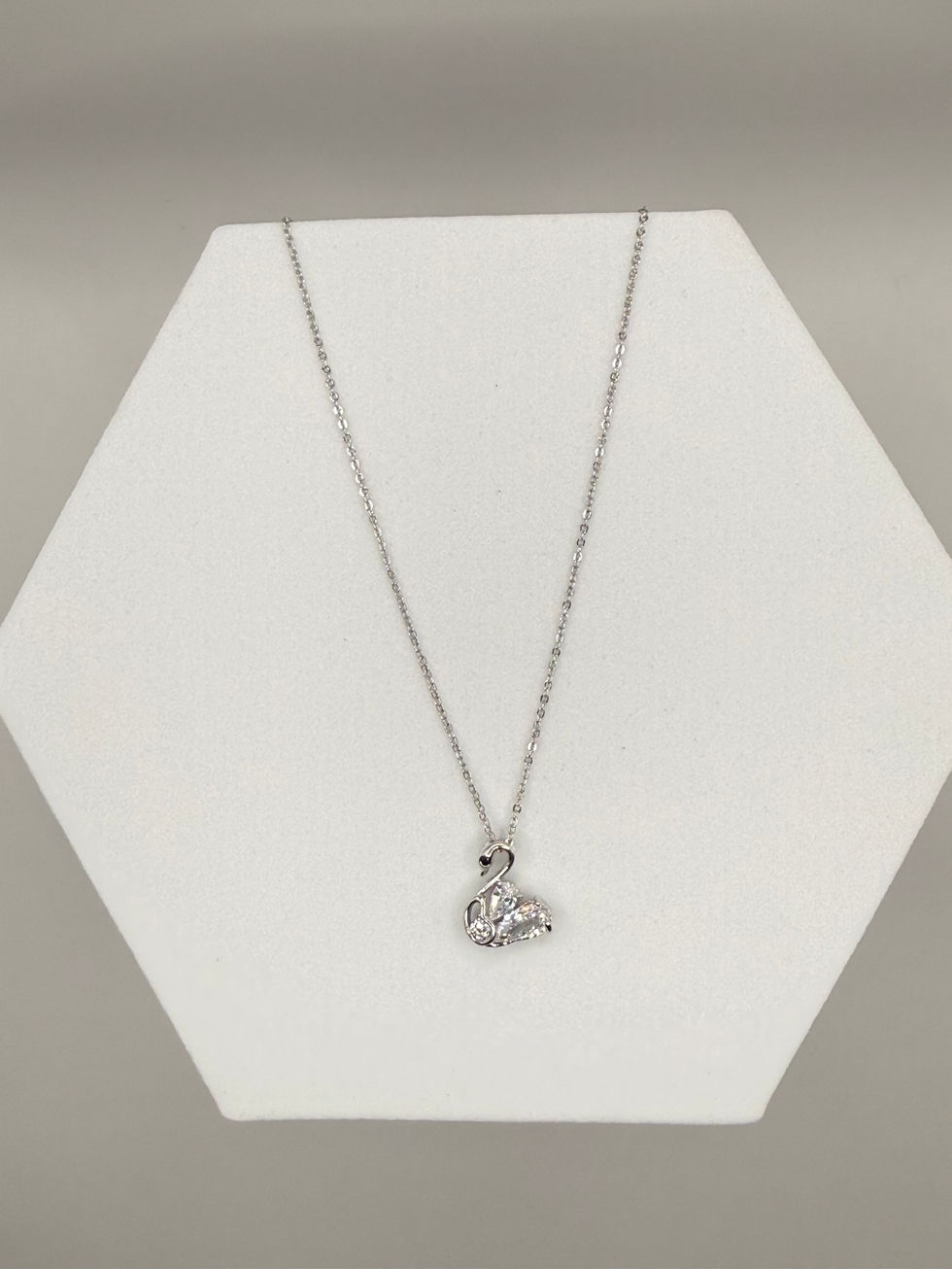 Silver swan pendant necklace displayed on a white hexagonal platform Lavish Jewellery