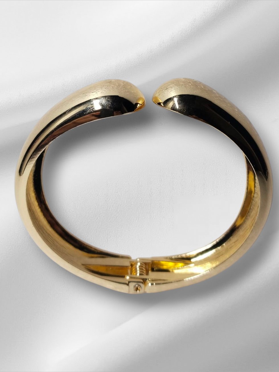 Golden bangle bracelet on a white surface, gold Lavish Jewellery.