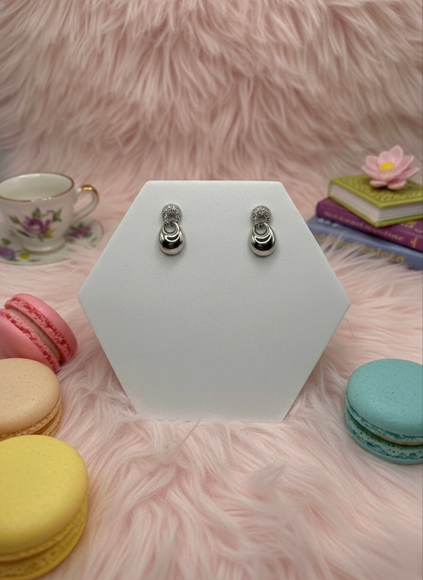 Elegant silver earrings on display with pink macarons and background.