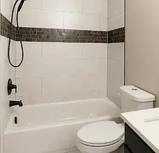 Modern bathroom with white tiled shower, black fixtures, toilet, and vanity.