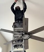 Skilled handyman on a ladder installing a new ceiling fan.
